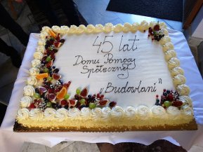 duży tort kwadratowy z białą masą śmietanową ozdobiony dużą ilością różnych owoców