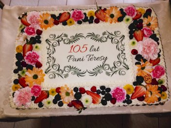 Tort udekorowany jeżynami, truskawkami i kwiatami. Na środku napis 105 lat Pani Teresy