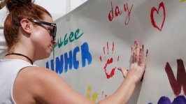 Powiększ obraz: dziewczyna odbijająca swoją umalowaną farbą dłoń na białej tablicy